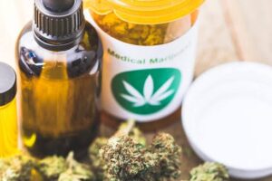 Medical marijuana bottle, cannabis oil dropper, and a jar labeled with a green leaf on a wooden surface, with cannabis buds nearby.