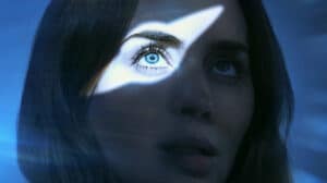 Close-up of a woman's face with a sharp white triangle of light across her blue eye, against a blue background.