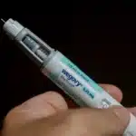 Injected Wegovy pen held in a hand with the needle exposed and blue label visible (Wegovy FlexTouch).