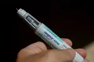 Injected Wegovy pen held in a hand with the needle exposed and blue label visible (Wegovy FlexTouch).