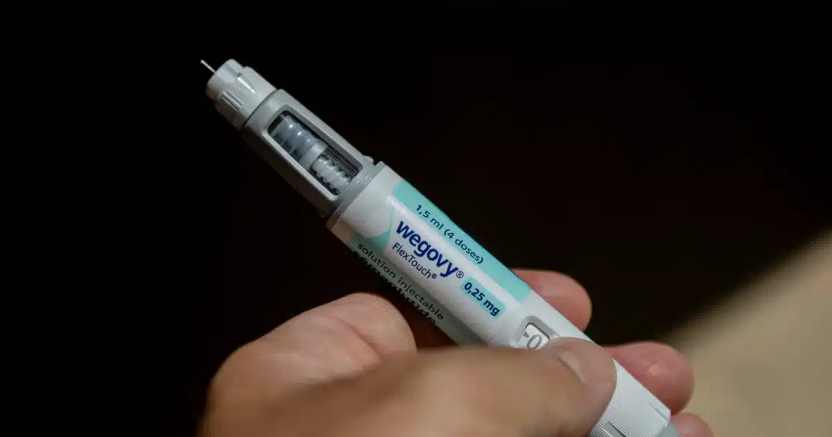 Injected Wegovy pen held in a hand with the needle exposed and blue label visible (Wegovy FlexTouch).