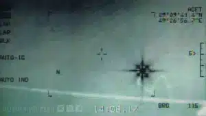 Close-up of an aircraft attitude indicator with horizon line, miniature airplane symbol, and compass-like markings on the right; a faint watermark and dashboard text are visible.