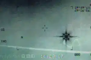 Close-up of an aircraft attitude indicator with horizon line, miniature airplane symbol, and compass-like markings on the right; a faint watermark and dashboard text are visible.