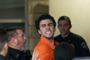 Man in an orange jumpsuit surrounded by several people indoors, some reaching toward him.