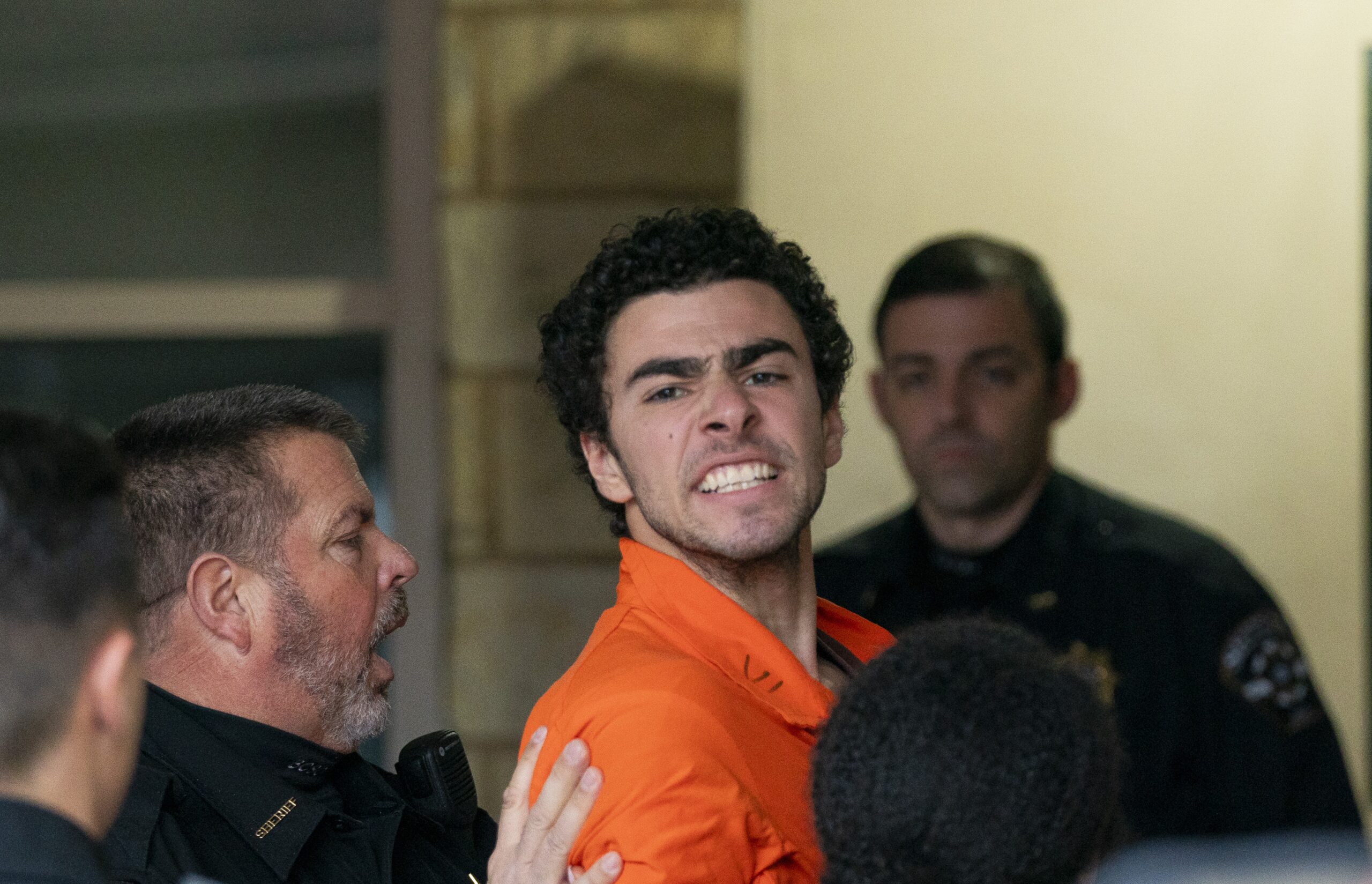 Man in an orange jumpsuit surrounded by several people indoors, some reaching toward him.