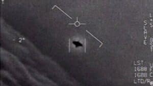 Grayscale medical image showing a circular crosshair marker with a diagonal line and a dark irregular shape near the lower center, plus measurement marks along the right edge.