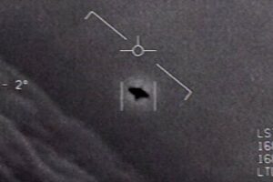 Grayscale medical image showing a circular crosshair marker with a diagonal line and a dark irregular shape near the lower center, plus measurement marks along the right edge.