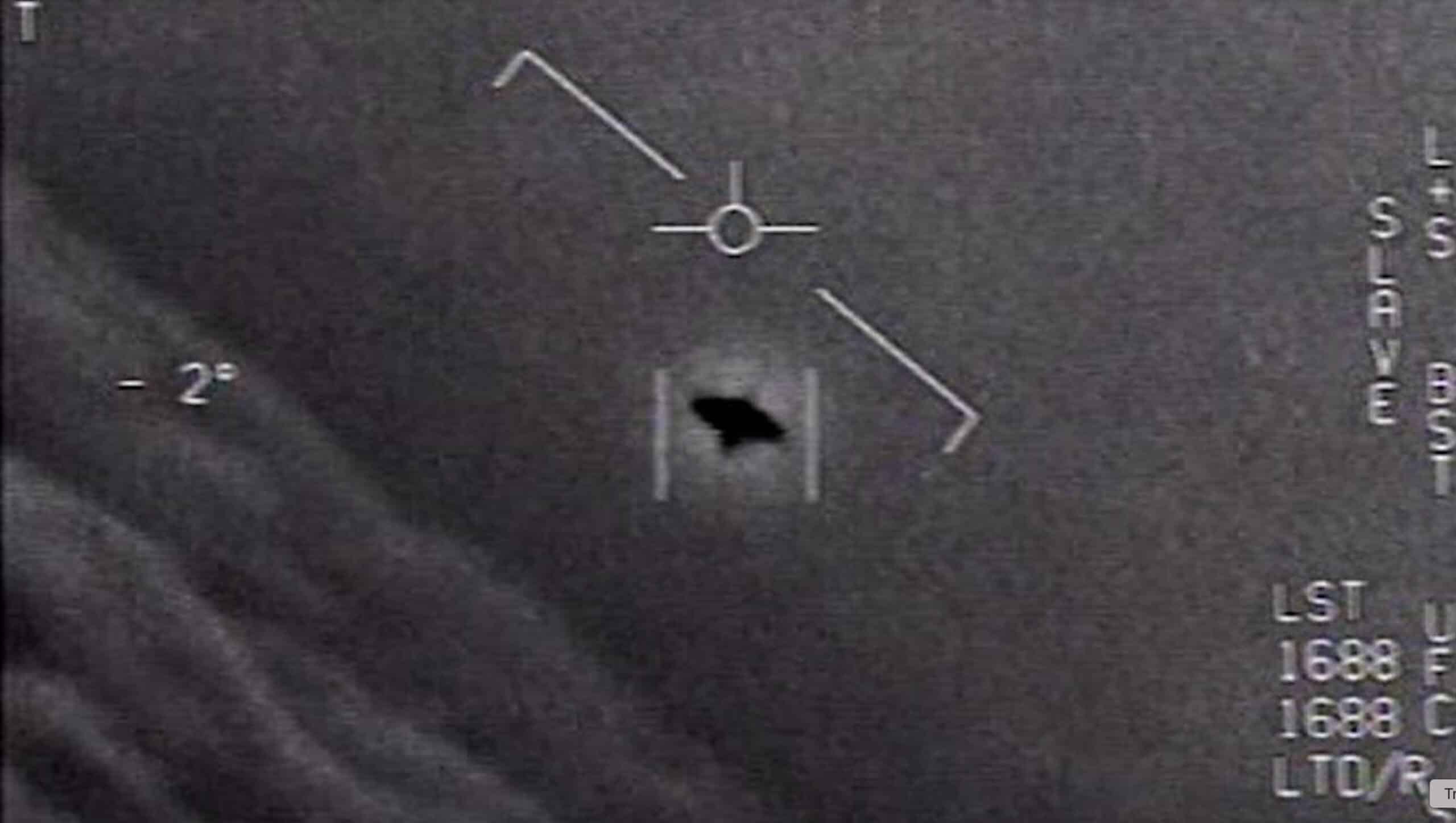 Grayscale medical image showing a circular crosshair marker with a diagonal line and a dark irregular shape near the lower center, plus measurement marks along the right edge.