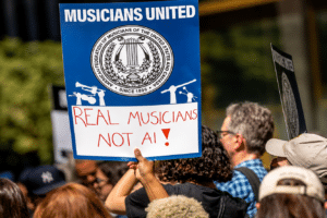 Protest sign: 'MUSICIANS UNITED' with emblem, reading 'REAL MUSICIANS NOT AI!' held by a crowd of protesters.