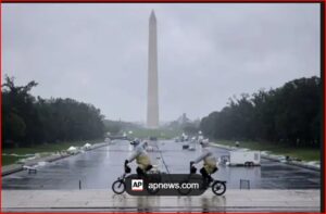 Two people ride small motorcycles on a wet, reflective pavement with the Washington Monument in the distance.