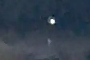 Bright white orb glowing in a dark night sky with a small faint shape beneath it (blurry image).