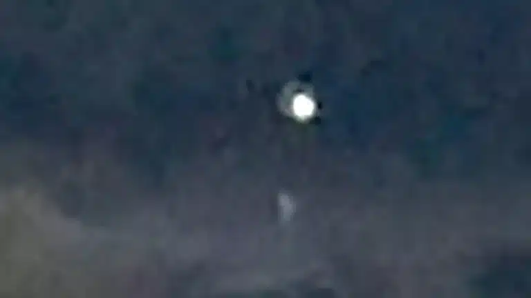 Bright white orb glowing in a dark night sky with a small faint shape beneath it (blurry image).