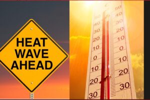 Yellow warning diamond sign reading 'HEAT WAVE AHEAD' beside a bright thermometer under a sunset sky, signaling extreme heat.