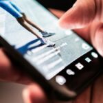 Close-up of a hand holding a smartphone while recording a runner's legs in motion.