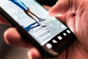 Close-up of a hand holding a smartphone while recording a runner's legs in motion.