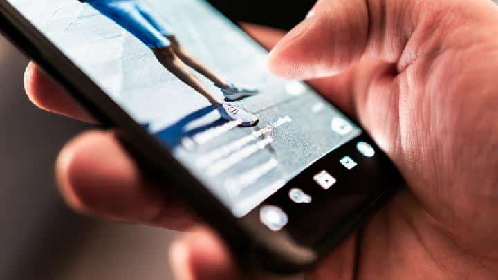 Close-up of a hand holding a smartphone while recording a runner's legs in motion.