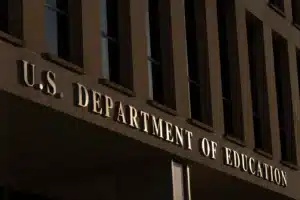 Facade of a government building with the illuminated sign 'U.S. Department of Education' along the entrance.