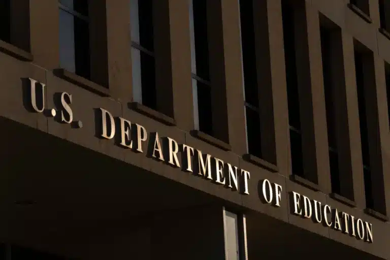 Facade of a government building with the illuminated sign 'U.S. Department of Education' along the entrance.