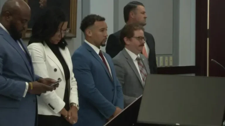 Group of professionally dressed people standing at a podium in a formal meeting room.