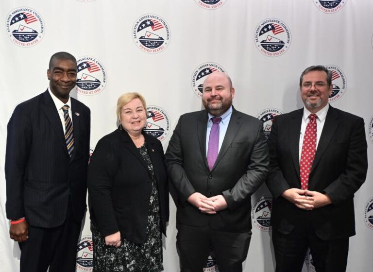 Members of the U.S. Election Assistance Commission standing in front of an EAC seal backdrop