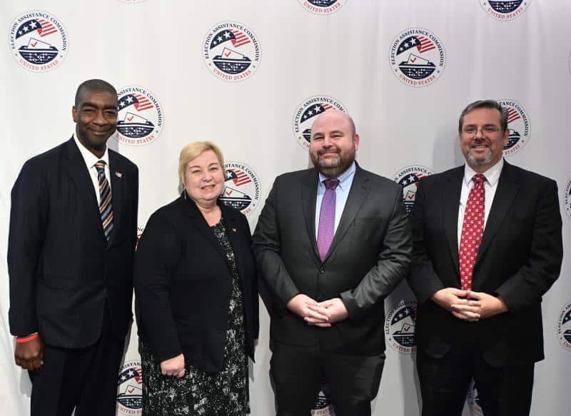 Members of the U.S. Election Assistance Commission standing in front of an EAC seal backdrop