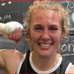 Smiling woman flexing her bicep after a workout with a chalkboard wall in the background