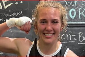 Smiling woman flexing her bicep after a workout with a chalkboard wall in the background