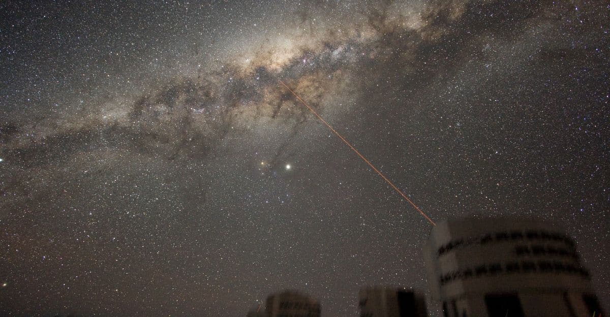 Star-filled night sky with the Milky Way arc and a red laser beam emitting from a rooftop observatory toward the stars.