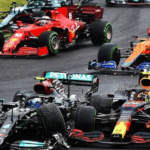 Close-packed Formula 1 cars racing on a track, with a Mercedes in the foreground and red Ferrari, orange McLaren, and blue cars nearby; tire spray visible on wet pavement.