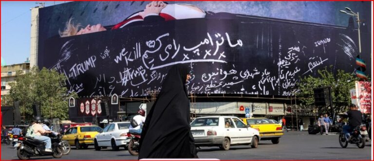 Busy city street with a large curved billboard covered in white cursive slogans, including ‘TRUMP’, as a woman in a black chador walks by among passing cars and motorcycles.