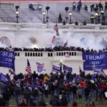 Crowd of Trump supporters on the Capitol steps with Trump 2020 banners and American flags.