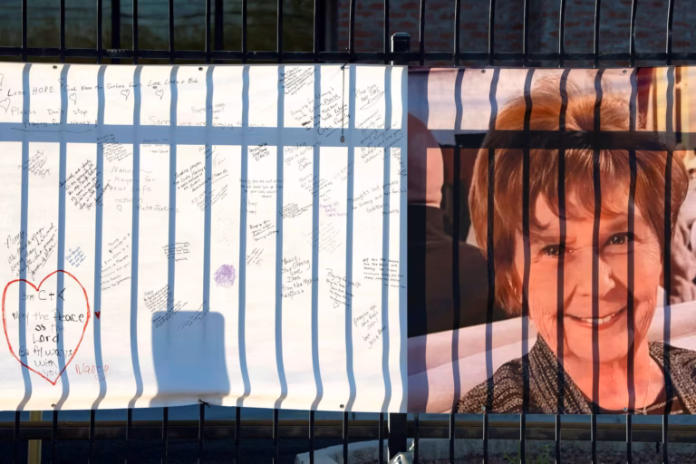 Banner on a fence showing a smiling woman on the right and white panels filled with handwritten messages and a red heart on the left—memorial-style display.