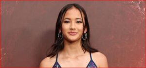 Young woman with dark hair wearing hoop earrings, facing camera against a brown background.