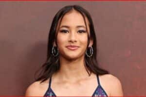 Young woman with dark hair wearing hoop earrings, facing camera against a brown background.