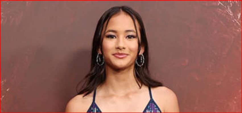 Young woman with dark hair wearing hoop earrings, facing camera against a brown background.