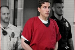 Man in a red jail jumpsuit escorted by two uniformed guards in a hallway
