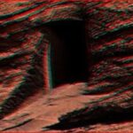 Rocky desert terrain with a dark cave opening carved into the red rock wall (anaglyph 3D effect).