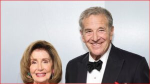 Smiling elderly couple dressed for a formal event; woman in a light-colored outfit with earrings, man in a black tuxedo and bow tie.
