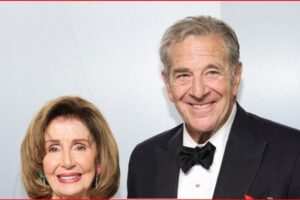 Smiling elderly couple dressed for a formal event; woman in a light-colored outfit with earrings, man in a black tuxedo and bow tie.