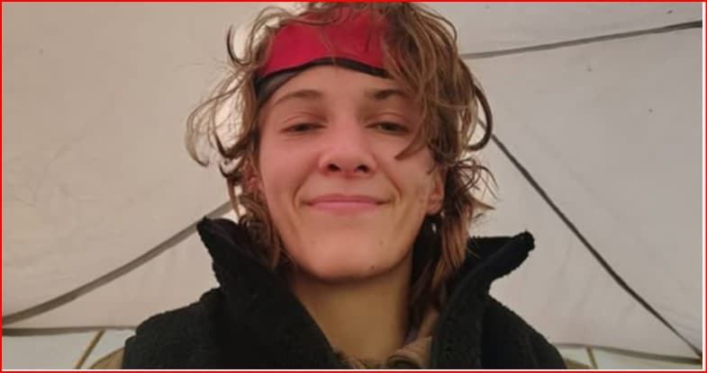 Woman with a red headband and tousled hair smiling at the camera inside a tent, wearing a black jacket.