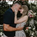 Couple embracing and about to kiss in a garden with pink and white flowers in the background.