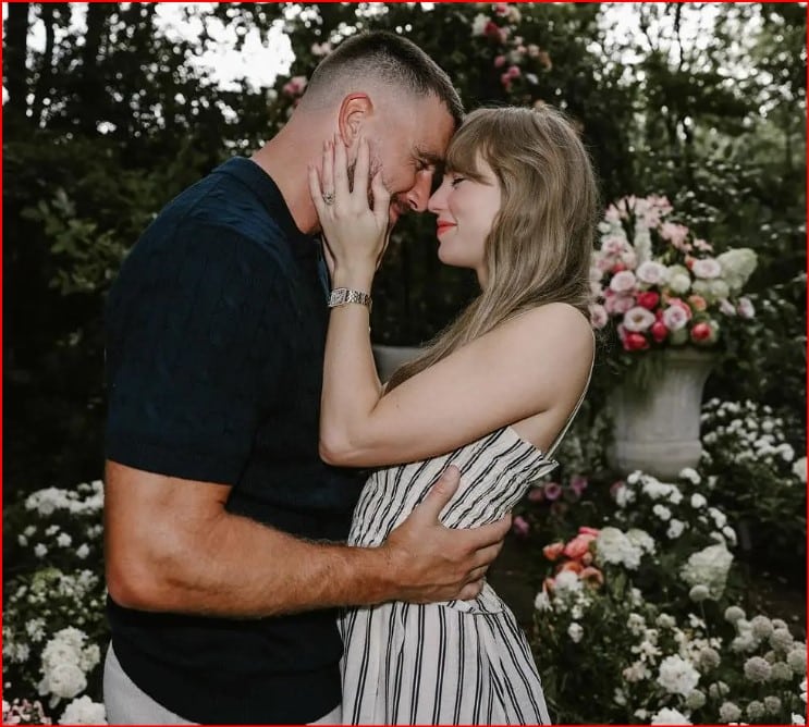 Couple embracing and about to kiss in a garden with pink and white flowers in the background.