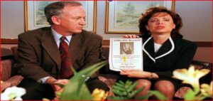 Man and woman in business attire sit on a couch, holding a $100,000 reward poster featuring a woman's photo in a waiting-room setting.