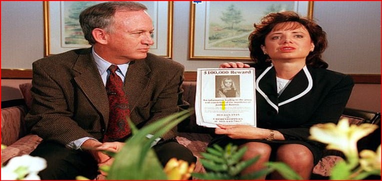 Man and woman in business attire sit on a couch, holding a $100,000 reward poster featuring a woman's photo in a waiting-room setting.