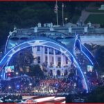 Nighttime view of the White House lawn with blue-lit arches, a large crowd, and a concert taking place on stage.