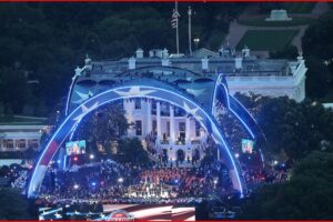 Nighttime view of the White House lawn with blue-lit arches, a large crowd, and a concert taking place on stage.