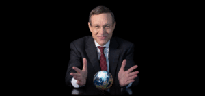 Smiling businessman in a dark suit holds a small globe on a table, appearing to present the Earth against a black background.