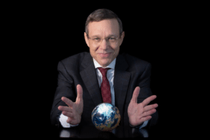 Smiling businessman in a dark suit holds a small globe on a table, appearing to present the Earth against a black background.