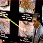 Man in a suit points to a forensic display showing bloodstain evidence in paper bags on a dark board.