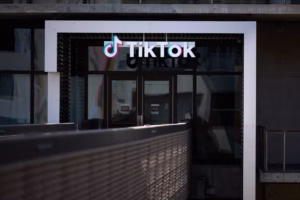 TikTok logo above glass doors of a building entrance, with a metal railing in the foreground.